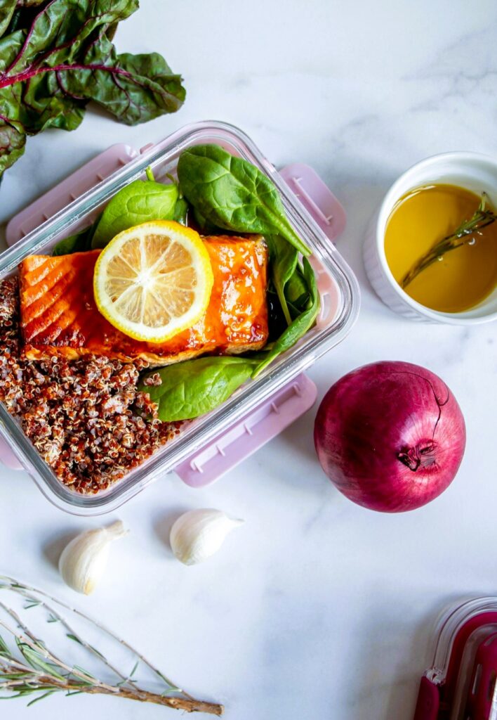 delicious-meal Healthy meal prep with salmon, quinoa, and spinach in a glass container, accompanied by ingredients and olive oil.